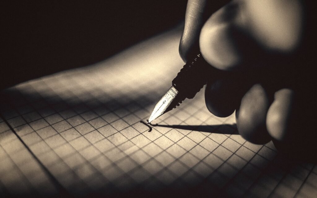Mano escribiendo con pluma sobre papel cuadriculado, con luz lateral