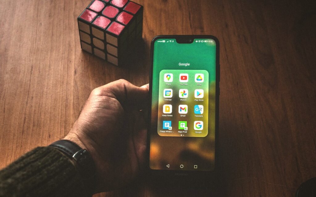 Mano sujetando un móvil con las aplicaciones de Google sobre una mesa de madera